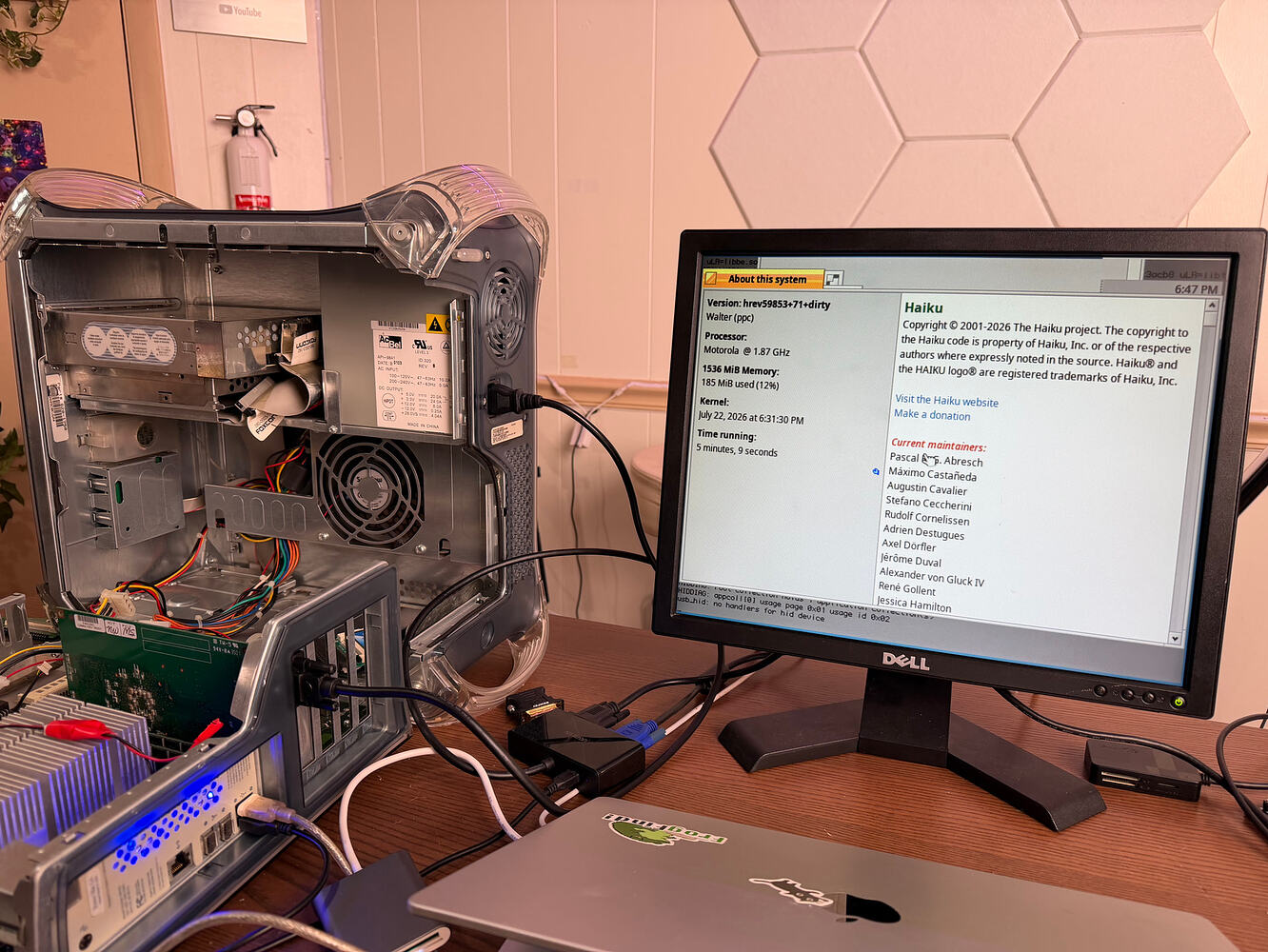 An open Power Mac G4 on a desk next to a monitor showing Haiku's About this system window on a 1.87 GHz Motorola PowerPC